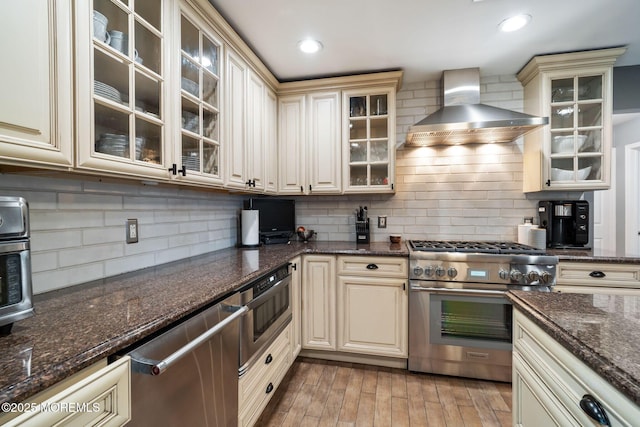 kitchen featuring appliances with stainless steel finishes, cream cabinets, backsplash, and wall chimney exhaust hood