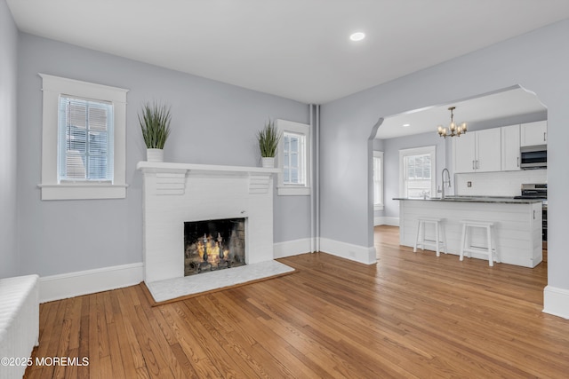 191 State Route 35, Red Bank, NJ 07701 - unfurnished living room featuring an inviting chandelier, arched walkways, a brick fireplace, baseboards, and light wood-style floors