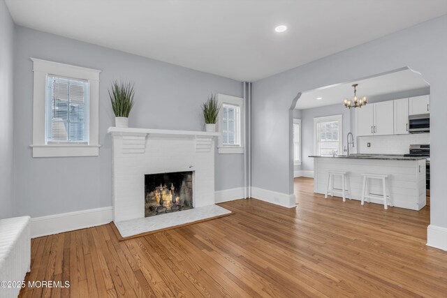 191 State Route 35, Red Bank, NJ 07701 - unfurnished living room featuring an inviting chandelier, arched walkways, a brick fireplace, baseboards, and light wood-style floors