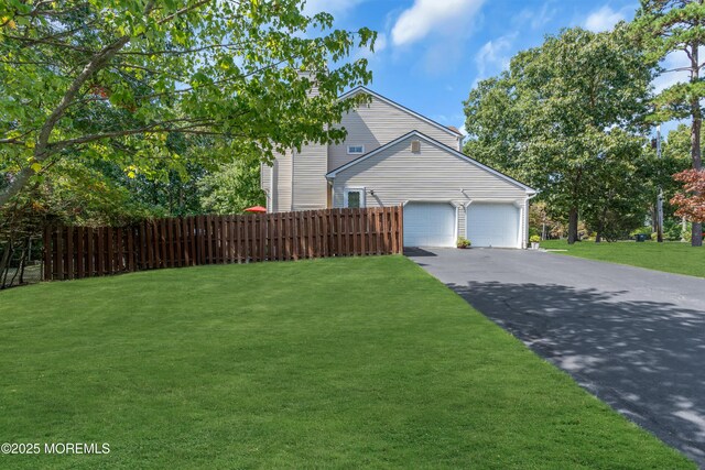 view of property exterior with fence, an attached garage, a yard, and aphalt driveway