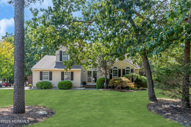 view of property hidden behind natural elements featuring roof with shingles and a front yard