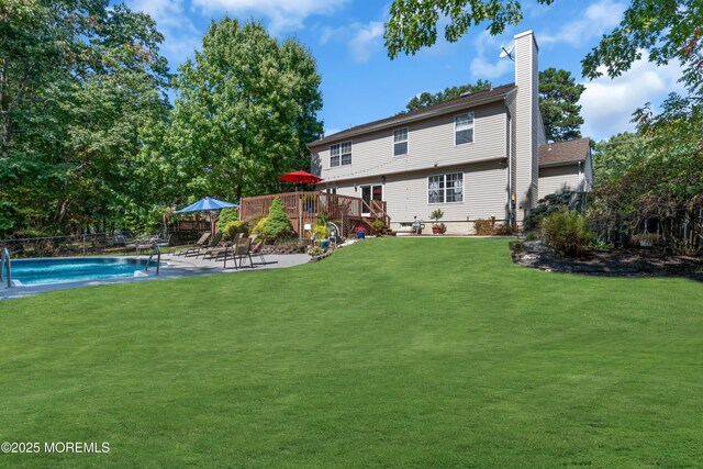 back of house featuring fence, a deck, a fenced in pool, a chimney, and a lawn