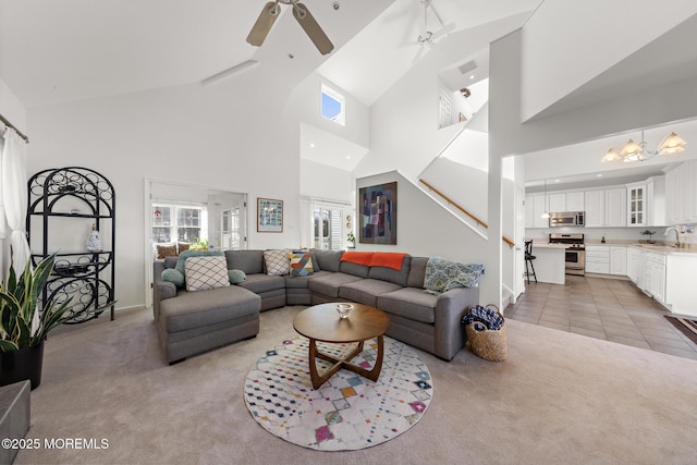 living room featuring stairs, light carpet, baseboards, high vaulted ceiling, and a ceiling fan