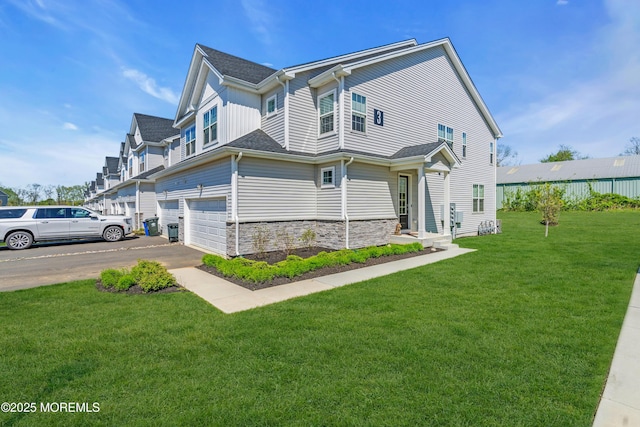 view of side of home featuring a yard, an attached garage, stone siding, and aphalt driveway