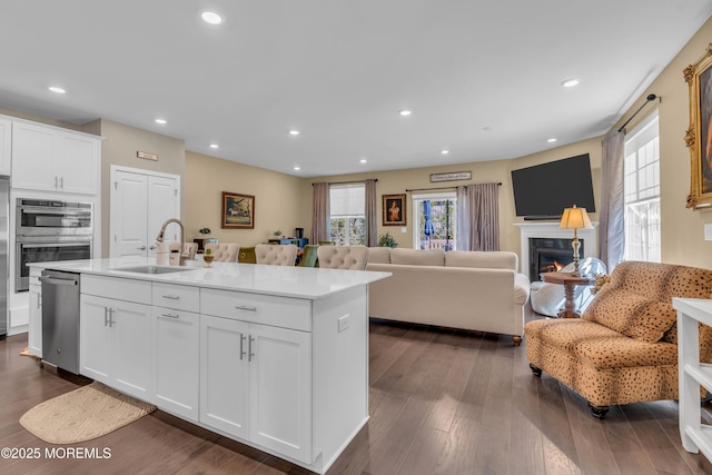 kitchen featuring a kitchen island with sink, open floor plan, white cabinetry, a sink, and stainless steel appliances