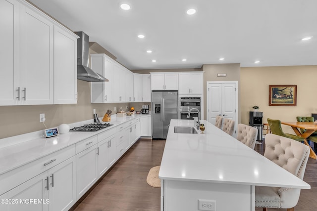 kitchen featuring appliances with stainless steel finishes, a sink, a breakfast bar area, wall chimney exhaust hood, and recessed lighting
