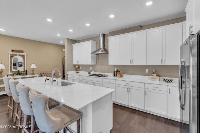kitchen featuring freestanding refrigerator, dark wood-style flooring, wall chimney range hood, white cabinets, and a sink