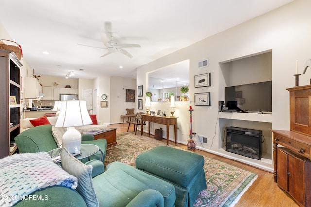 living room featuring light wood-style floors, visible vents, a ceiling fan, and a glass covered fireplace