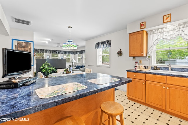kitchen featuring visible vents, light floors, a kitchen breakfast bar, ceiling fan, and a sink
