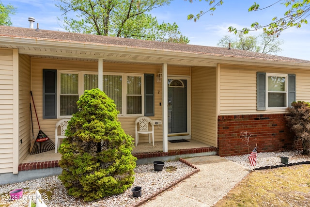 entrance to property featuring covered porch, a shingled roof, and brick siding