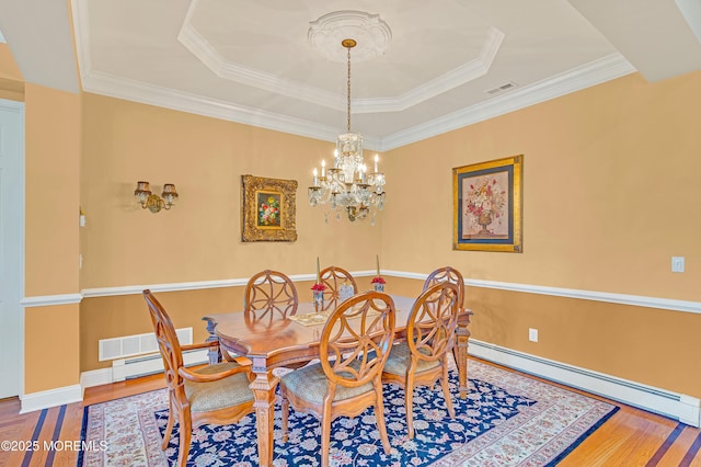dining space with a notable chandelier, baseboard heating, wood finished floors, a tray ceiling, and visible vents