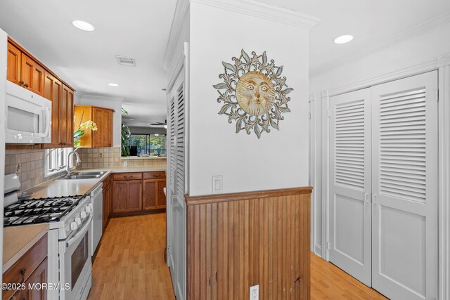 kitchen with visible vents, crown molding, a sink, light wood-style floors, and white appliances