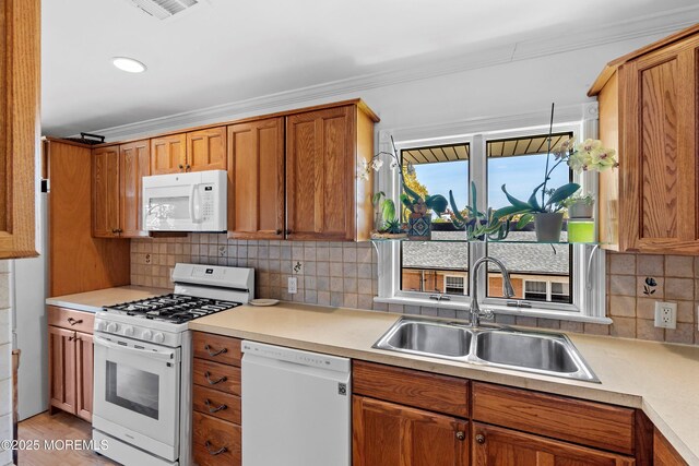 kitchen with a sink, white appliances, light countertops, brown cabinetry, and ornamental molding