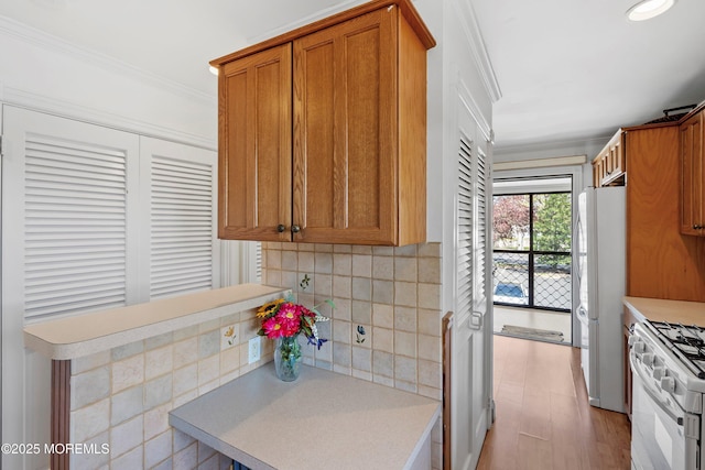 kitchen featuring crown molding, tasteful backsplash, brown cabinets, light countertops, and white appliances