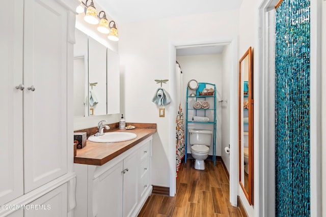 bathroom featuring toilet, baseboards, wood finished floors, and vanity