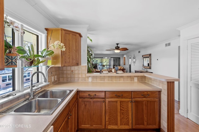kitchen featuring ornamental molding, a peninsula, ceiling fan, light countertops, and a sink