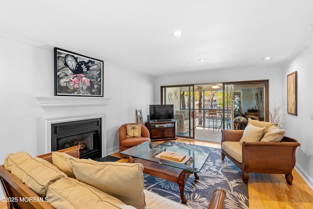 living room featuring crown molding, recessed lighting, a glass covered fireplace, and wood finished floors