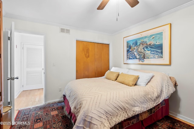 bedroom featuring baseboards, wood finished floors, visible vents, ornamental molding, and a closet