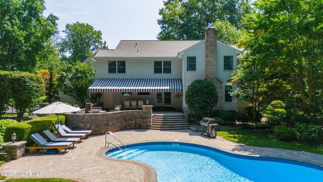 rear view of property with a patio, a chimney, and an outdoor pool