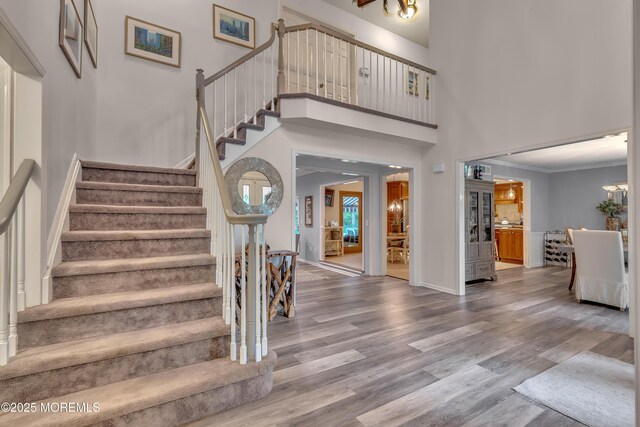 entrance foyer with ornamental molding, stairs, wood finished floors, baseboards, and a high ceiling