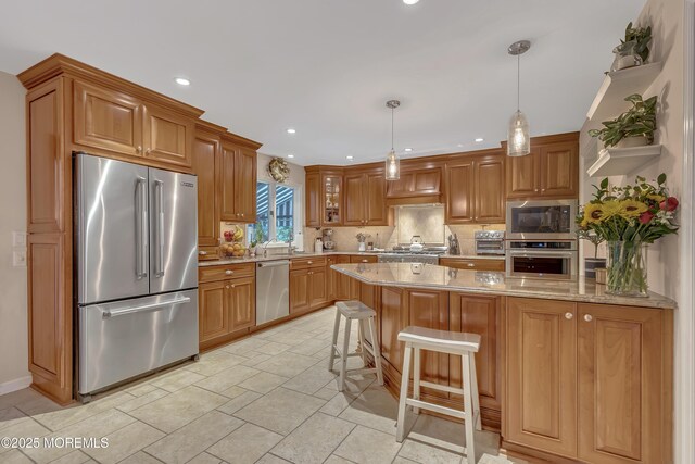 kitchen featuring brown cabinetry, a peninsula, tasteful backsplash, appliances with stainless steel finishes, and decorative light fixtures
