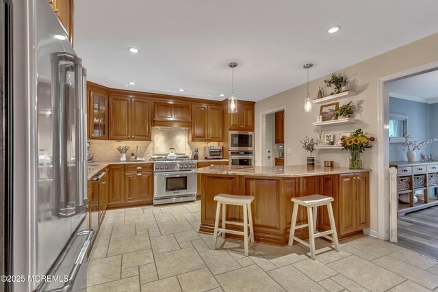 kitchen featuring decorative backsplash, a peninsula, light stone countertops, a breakfast bar area, and high quality appliances