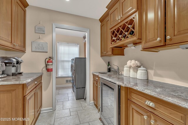 kitchen with stone tile flooring, beverage cooler, baseboards, light stone counters, and a sink