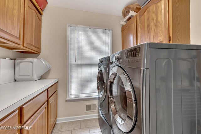 clothes washing area featuring visible vents, washing machine and clothes dryer, cabinet space, light tile patterned floors, and baseboards