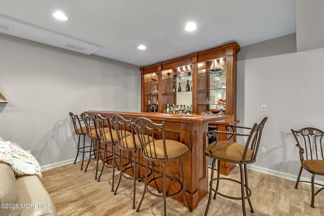 bar with baseboards, a bar, recessed lighting, and light wood-style flooring