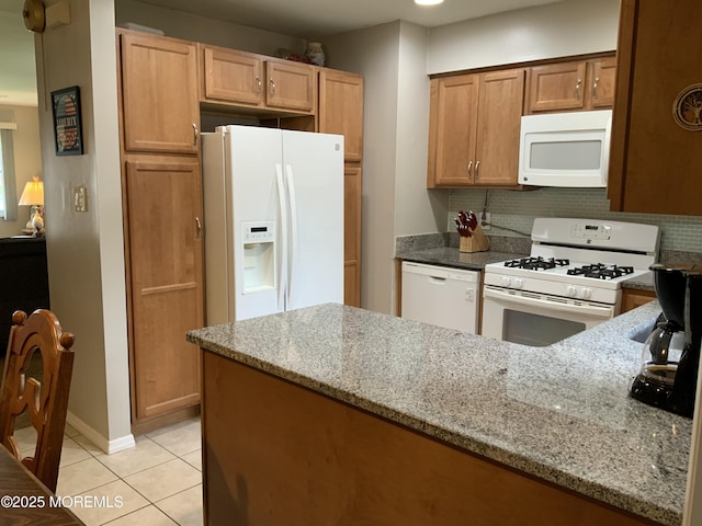 kitchen with light tile patterned flooring, light stone counters, white appliances, a peninsula, and tasteful backsplash