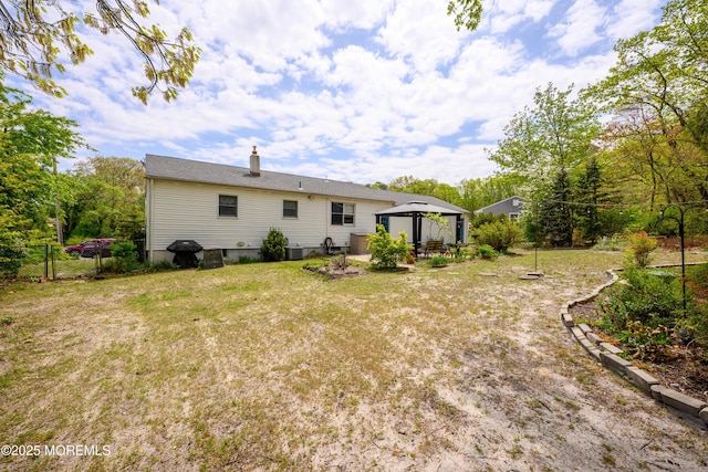 back of property featuring a chimney, central AC unit, a gazebo, fence, and a yard