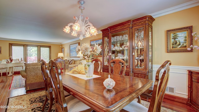 dining room with ornamental molding, light wood-style flooring, visible vents, and a chandelier