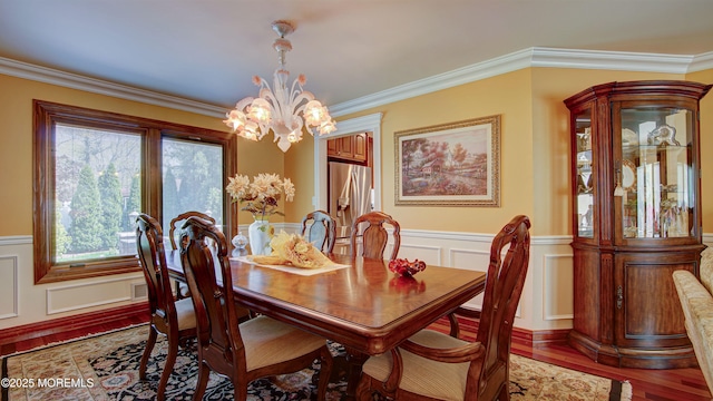 dining area with crown molding, wainscoting, wood finished floors, and a chandelier
