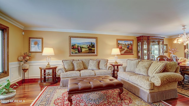 living area with a chandelier, ornamental molding, wood finished floors, and a wainscoted wall