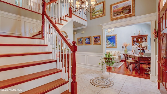 staircase featuring tile patterned flooring, wainscoting, a towering ceiling, and a notable chandelier