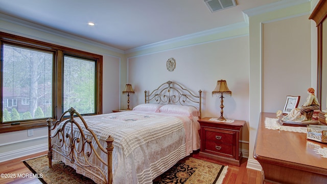 bedroom with crown molding, baseboards, wood finished floors, and visible vents
