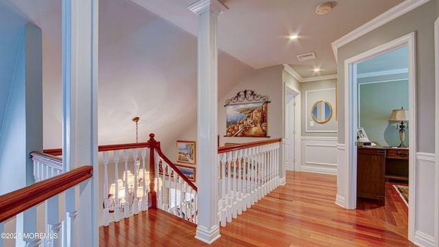 hall with visible vents, ornamental molding, a decorative wall, light wood-style floors, and an upstairs landing
