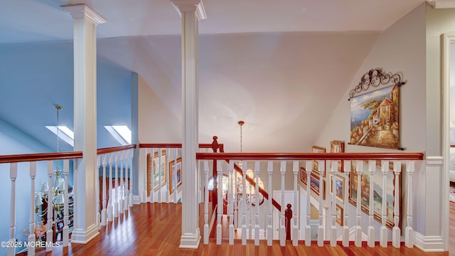 corridor with ornate columns, wood finished floors, and vaulted ceiling with skylight