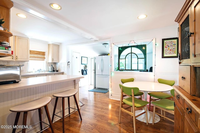 kitchen with light wood-style floors, light countertops, a breakfast bar area, freestanding refrigerator, and tasteful backsplash
