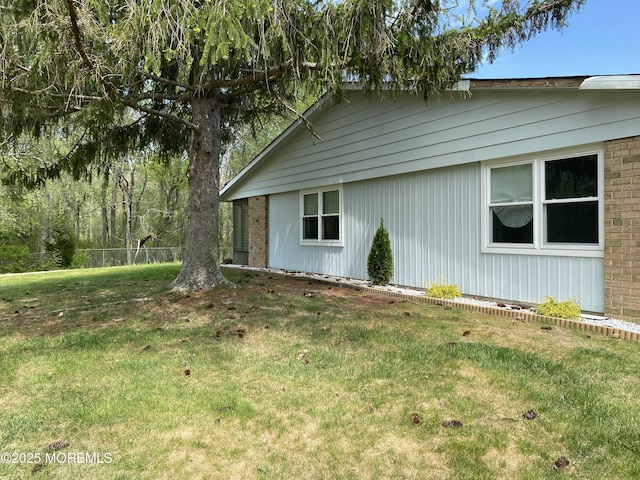 view of property exterior featuring brick siding, fence, and a yard