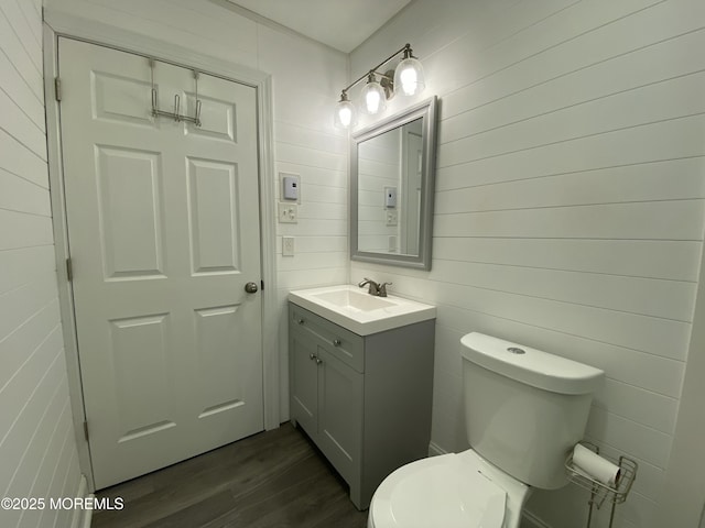 half bathroom with toilet, wood finished floors, and vanity