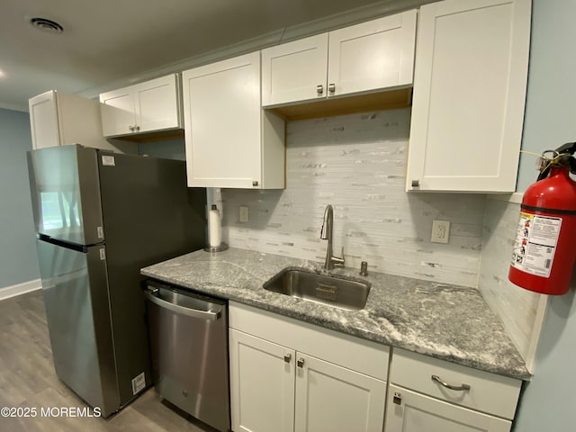 kitchen with light stone countertops, white cabinets, a sink, appliances with stainless steel finishes, and backsplash