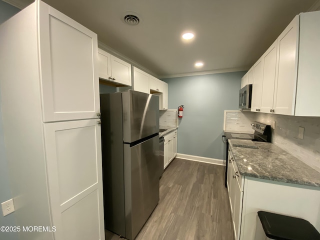 kitchen featuring dark stone countertops, stainless steel appliances, baseboards, white cabinetry, and wood finished floors