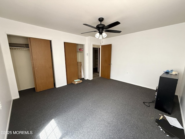 unfurnished bedroom with two closets, baseboards, and ceiling fan