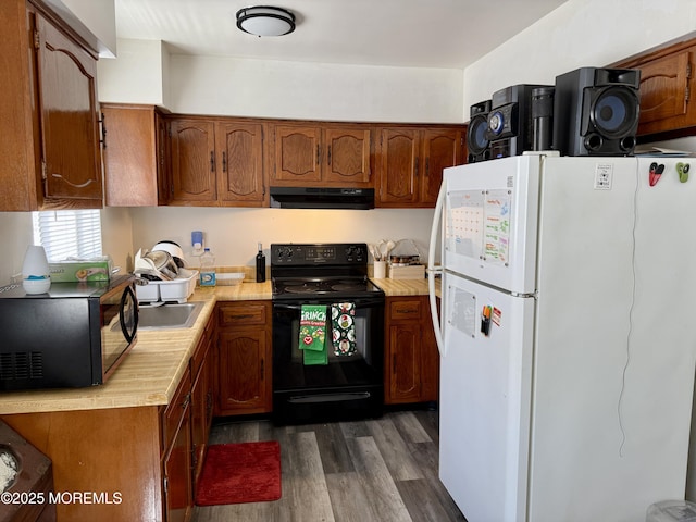 kitchen with brown cabinets, ventilation hood, light countertops, dark wood finished floors, and black appliances