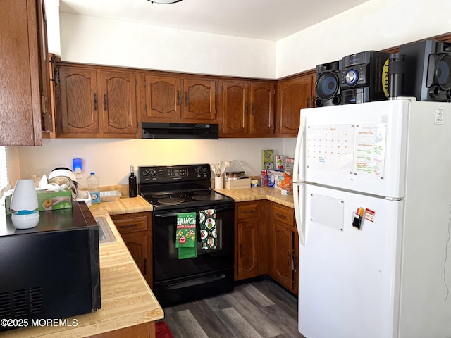 kitchen with brown cabinets, dark wood-style flooring, black electric range, freestanding refrigerator, and under cabinet range hood