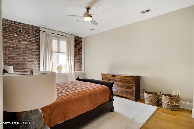 bedroom with brick wall, wood finished floors, baseboards, and a ceiling fan