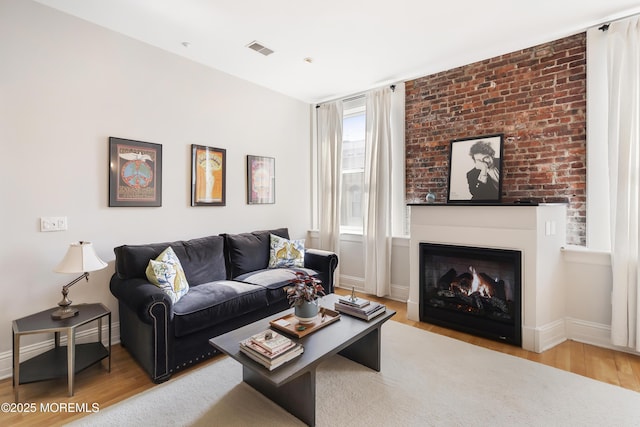 living room featuring wood finished floors, baseboards, and a warm lit fireplace