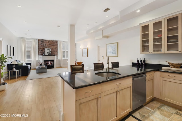 kitchen featuring stainless steel dishwasher, a sink, light brown cabinetry, a peninsula, and open floor plan