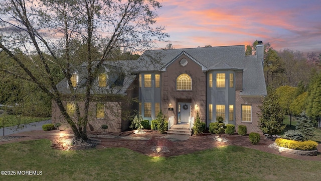 view of front of property featuring a shingled roof, a chimney, brick siding, and a front yard